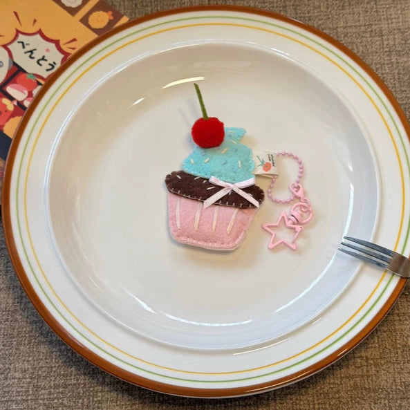 Decorative cupcake plushie on a plate with a fork, on a textured surface.