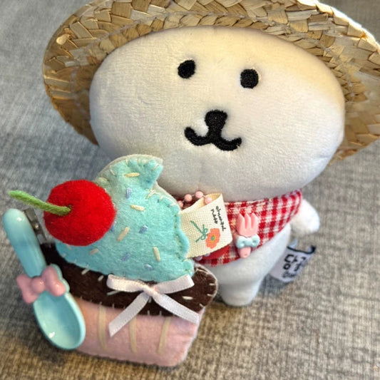 Plush toy resembling a rice cake with a straw hat and ice cream, on a textured surface.