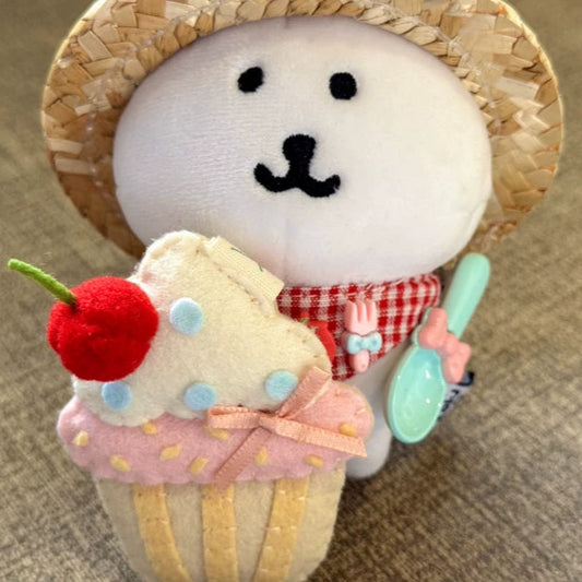 Toy bear wearing a straw hat holding a cupcake with a cherry on top.