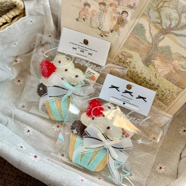 Set of decorative hair clips with ribbons in a clear bag, placed on a textured fabric surface.