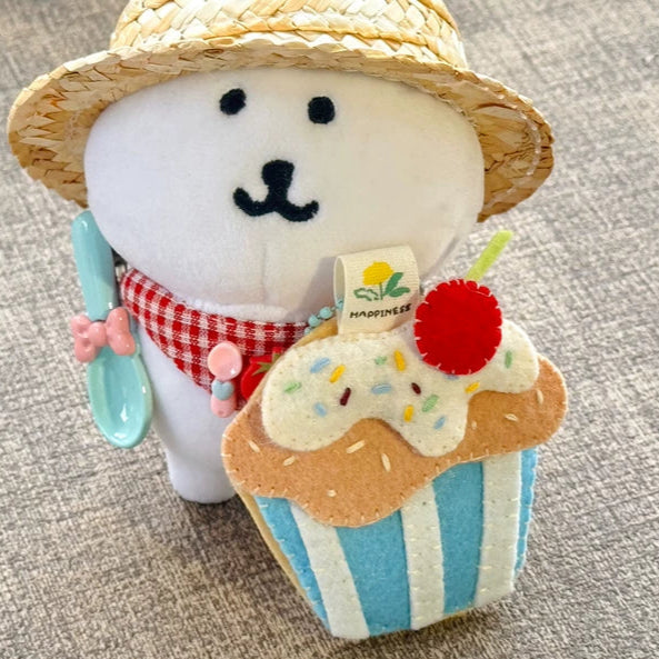Plush toy resembling a snowman with a straw hat and cupcake, sitting on a textured surface.